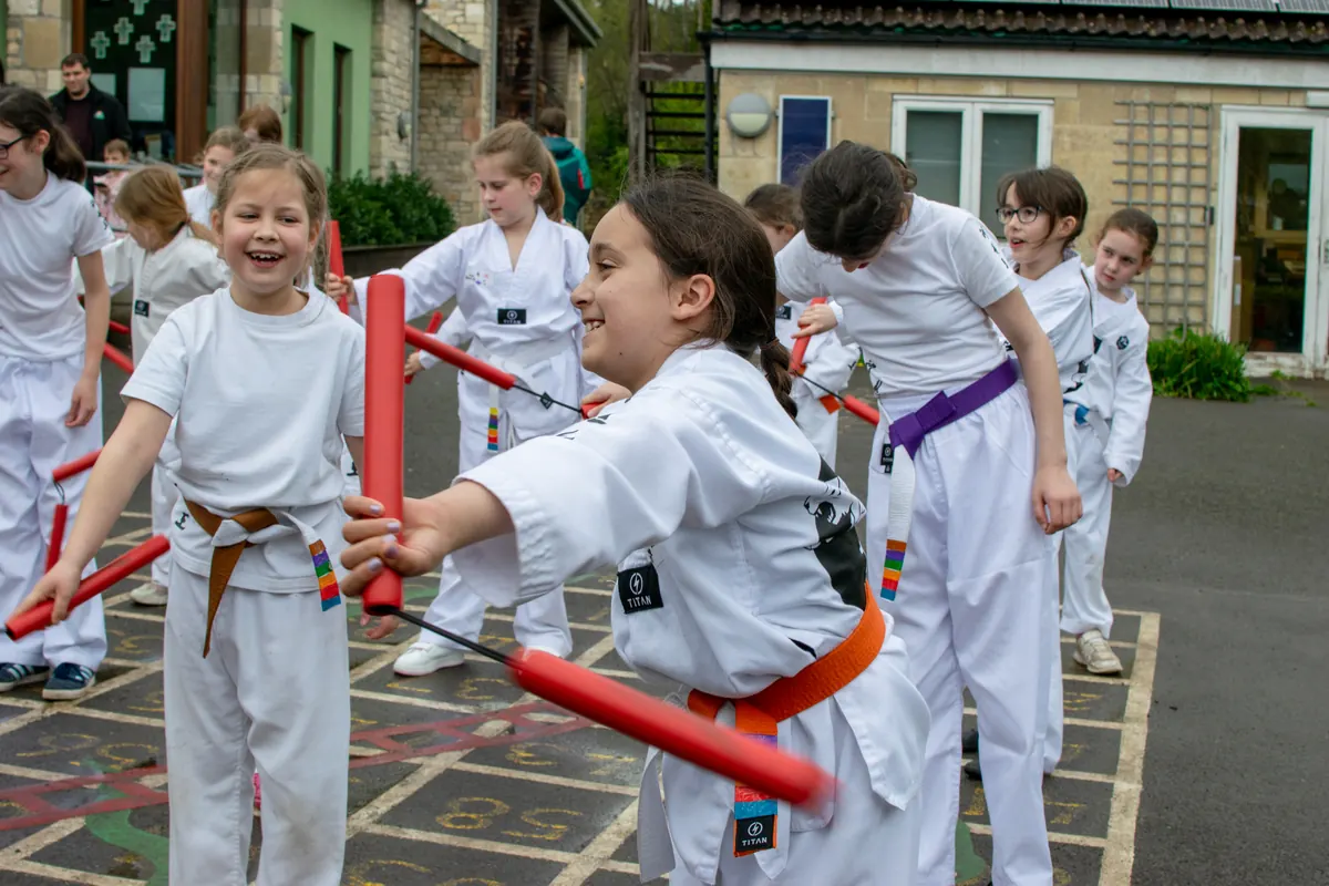An older student laughing with a younger student as they practise with foam nunchaku